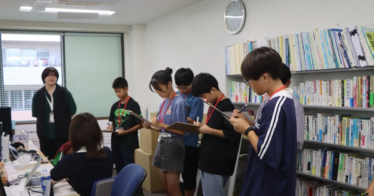 オフィスで説明を聞きながらメモを取る生徒たち