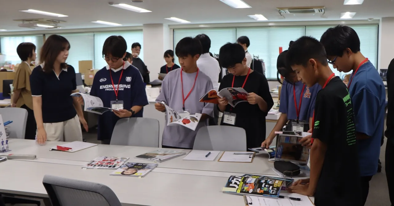 書棚の前で掲載誌を手に取り、説明を聞く生徒たち