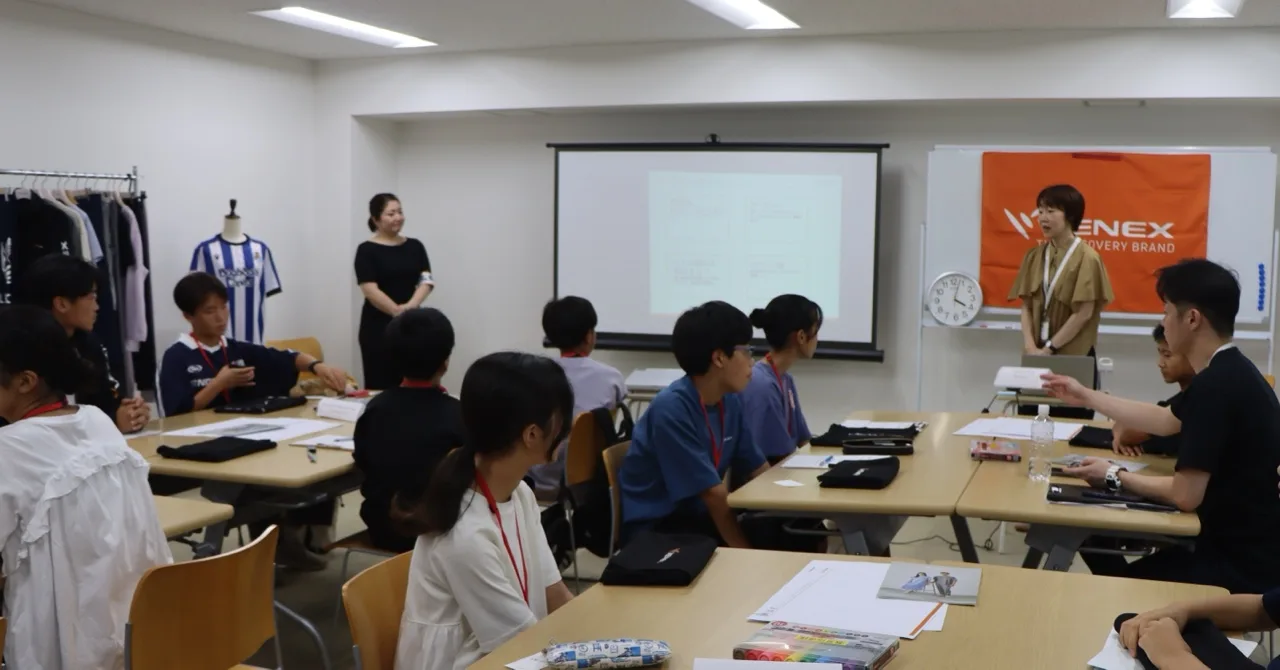 机に広げたアイデアシートに向かう生徒と、そばで見守る社員