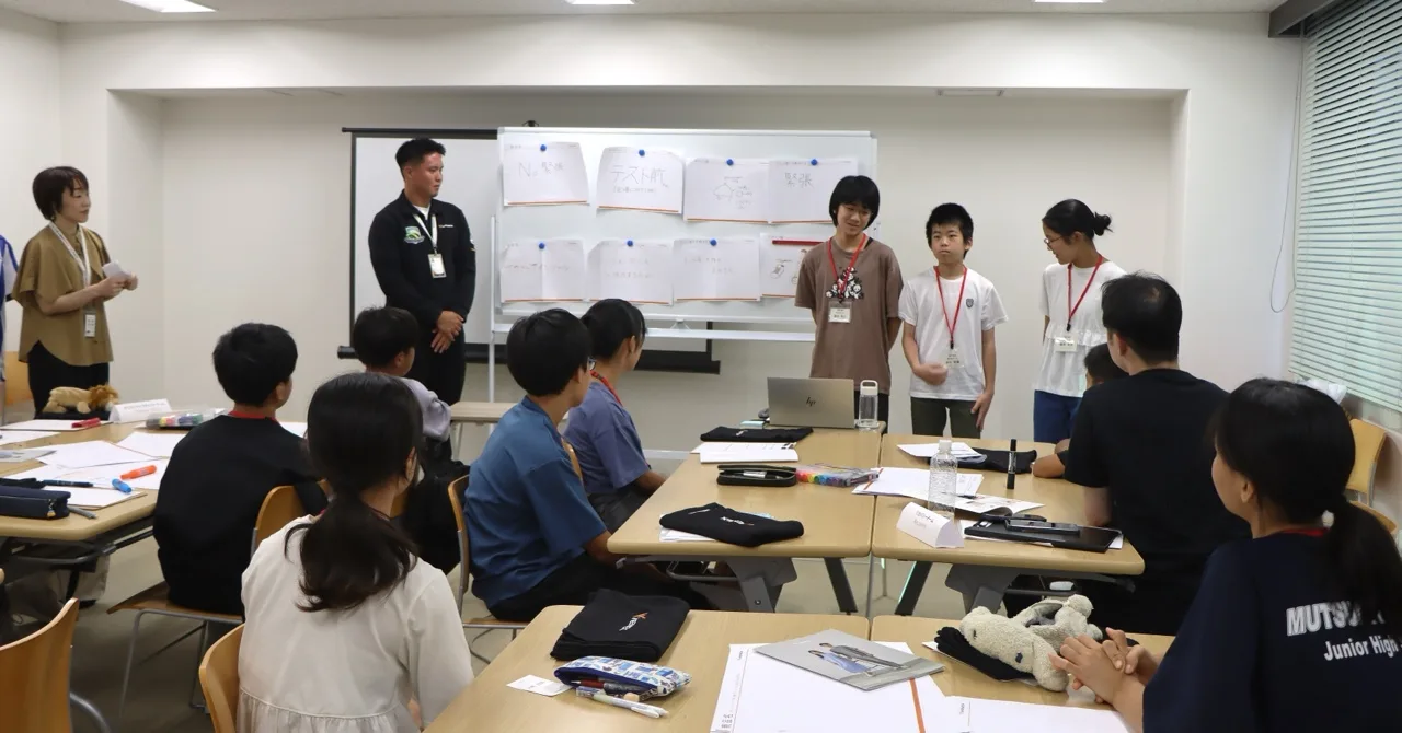 ホワイトボードに並んだ企画書を前に発表する生徒たち