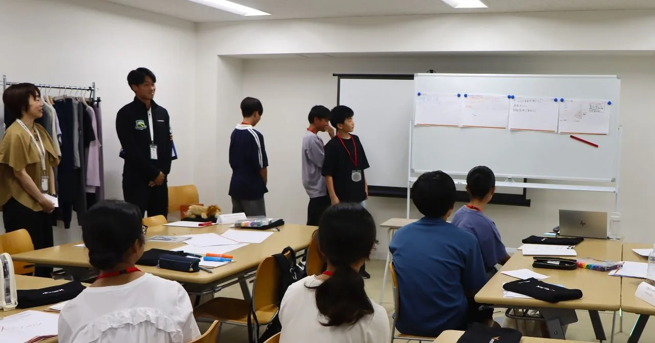 発表を見守る社員と、会場に立つ生徒たち