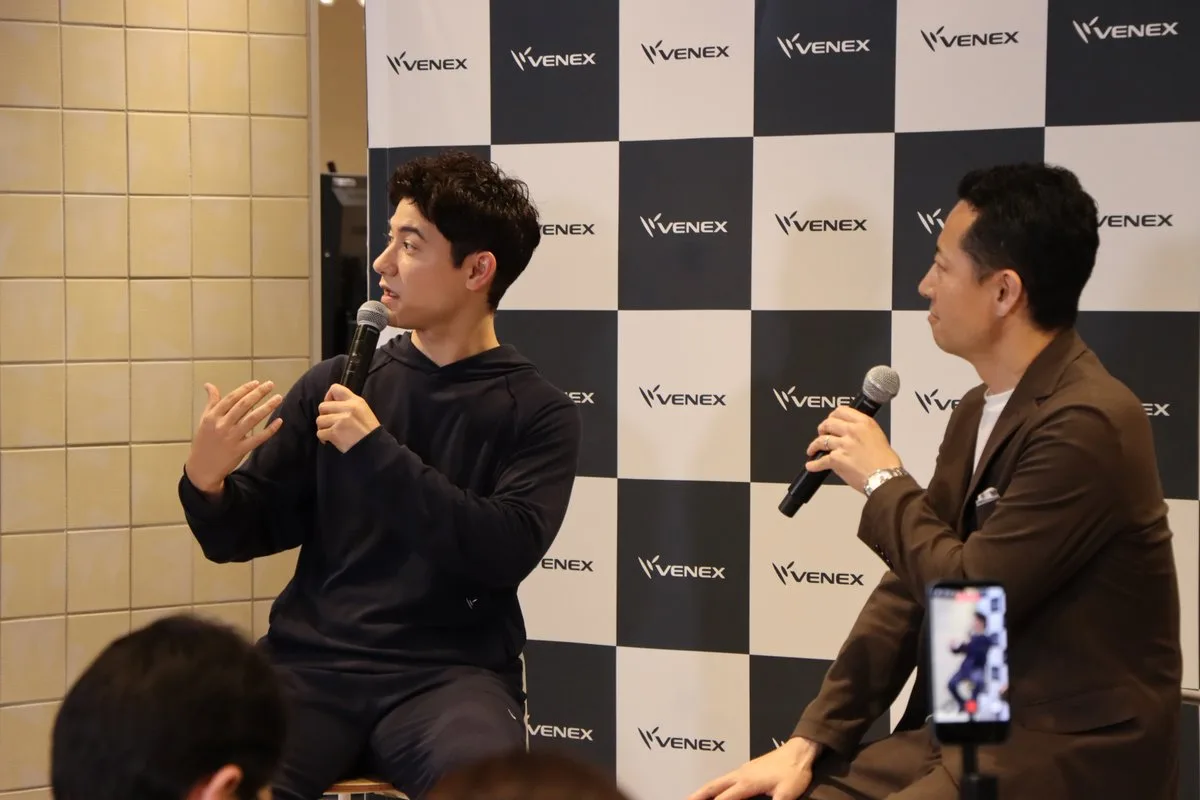 VENEXのバックパネルの前でトークする国山ハセンさんと当社取締役COOの菱沼信之