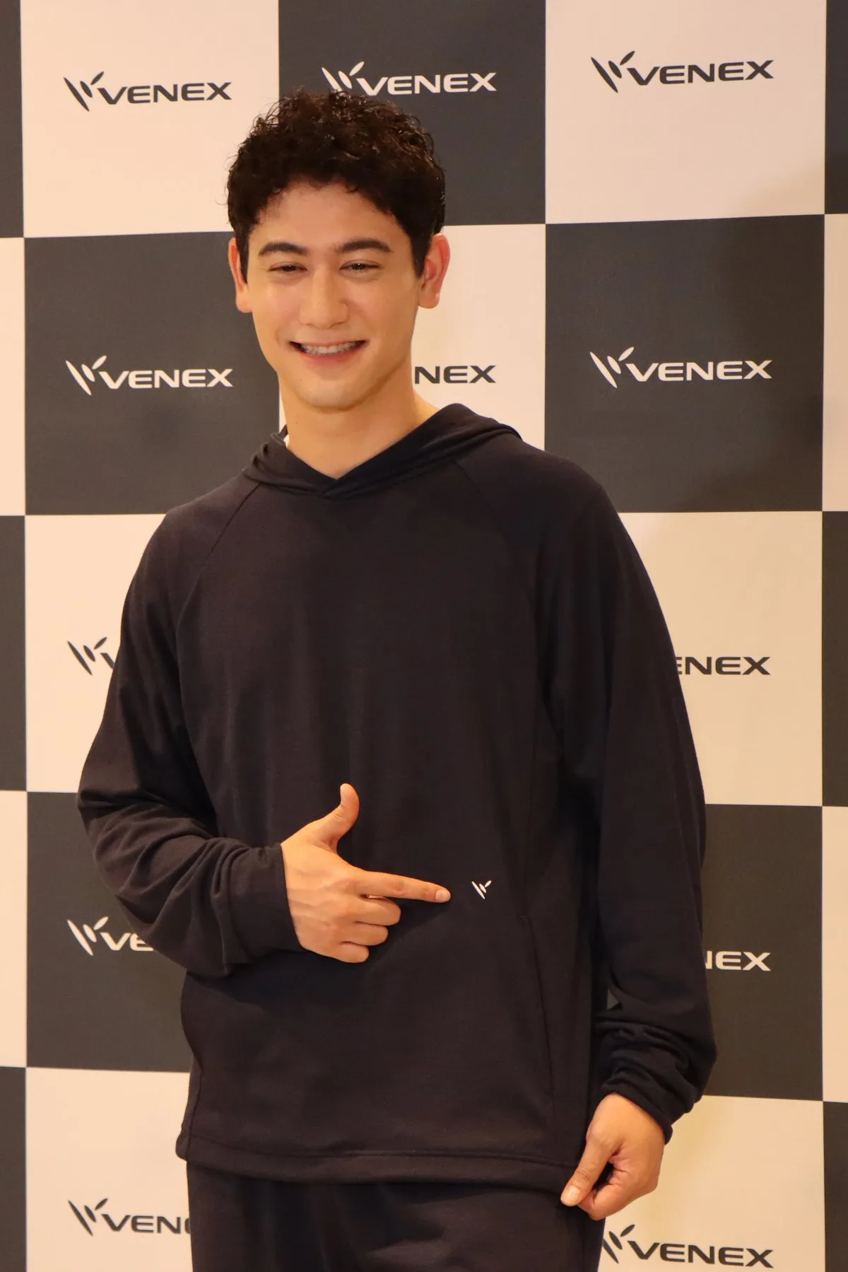 ネイビーのフーディの胸元のVENEXロゴを指さして笑顔の国山ハセンさん