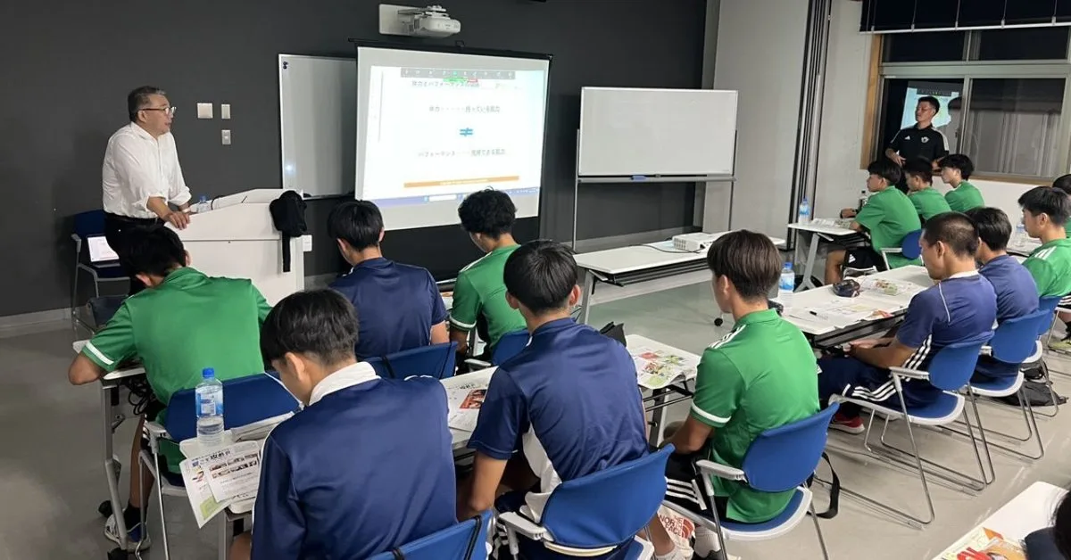 スクリーンの前で講義するVENEX担当者と、机に向かうトップチームの選手たち