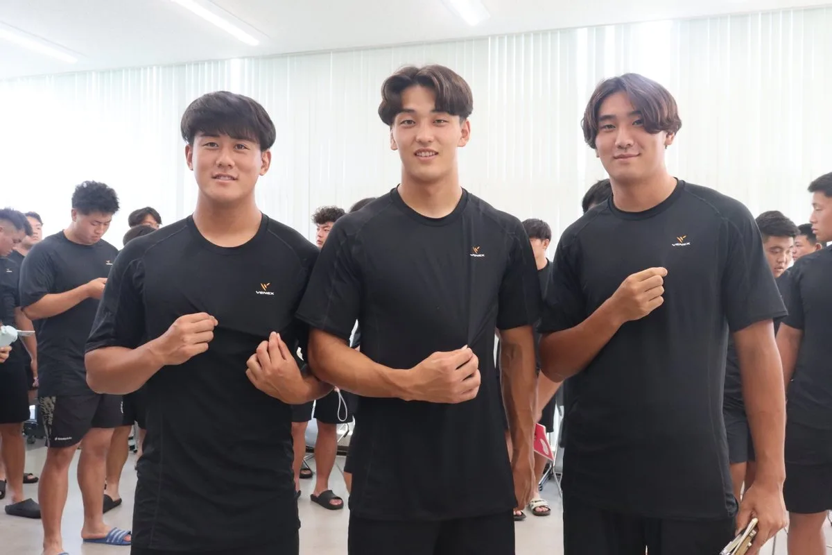 VENEXのリカバリーウェアを着用し、胸元のロゴを指さす明治大学ラグビー部の選手3人