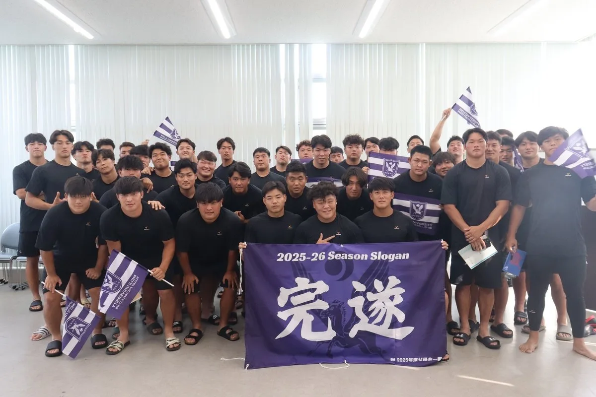 「完遂」のスローガン旗を囲む明治大学ラグビー部の選手たちの集合写真