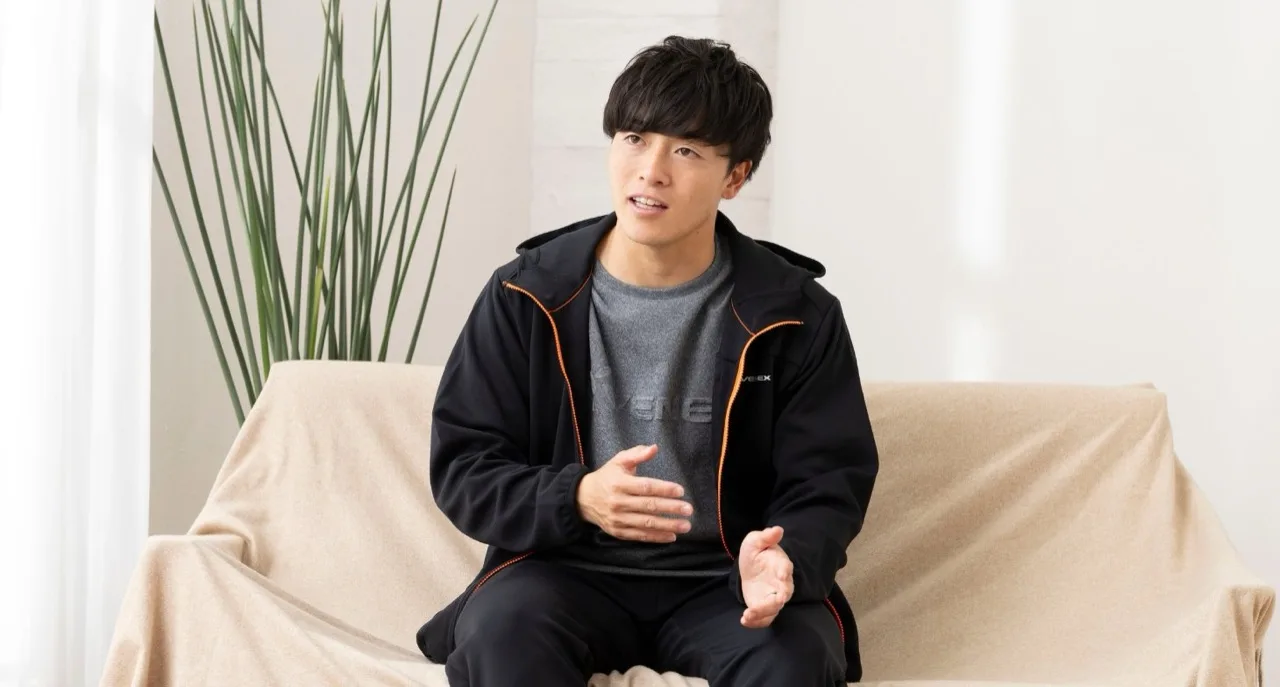 ソファに座り、身ぶりを交えて話すVENEXウェア姿の相馬勇紀選手